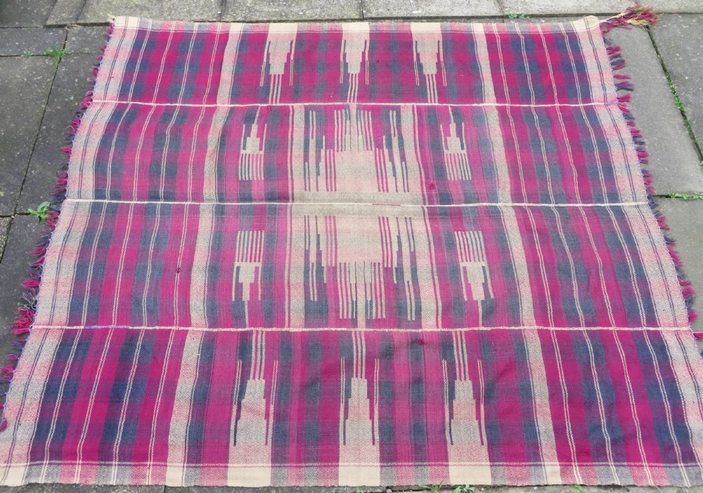 A rectangular flat-woven wool textile featuring crimson, navy, and cream geometric checked patterns with fringed ends. View IV