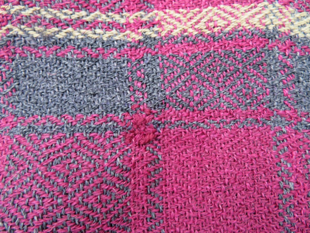 A rectangular flat-woven wool textile featuring crimson, navy, and cream geometric checked patterns with fringed ends. View X