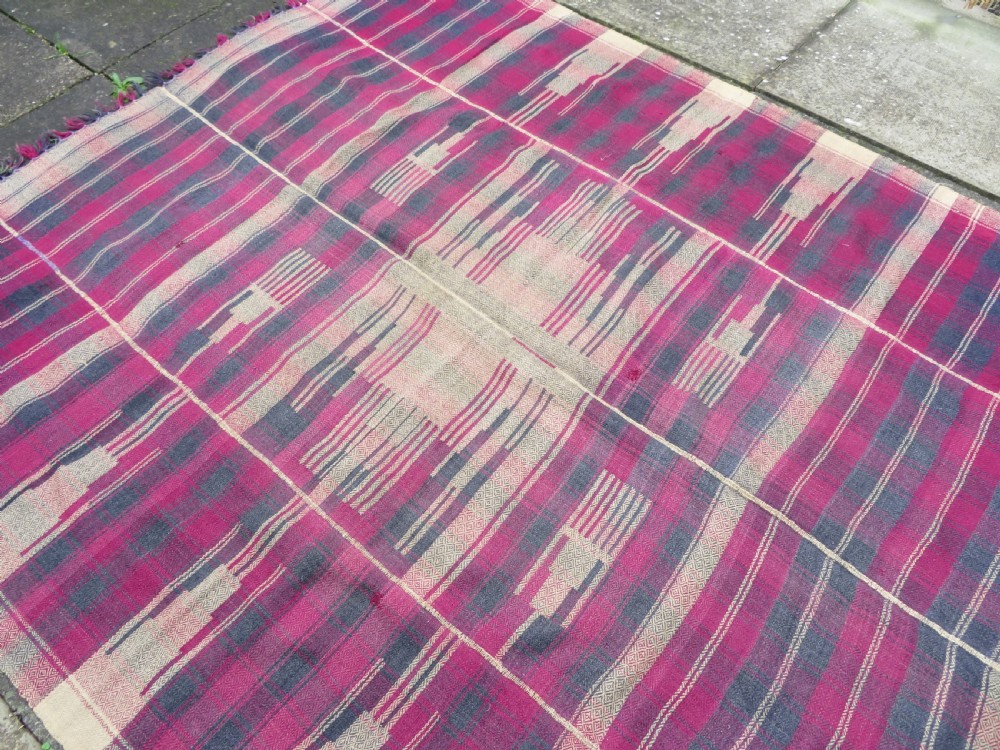 A rectangular flat-woven wool textile featuring crimson, navy, and cream geometric checked patterns with fringed ends. View XVI