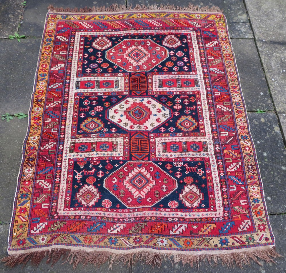An antique late 19th-century Caucasian Kuba Konagkend wool rug featuring red geometric medallions set against a dark navy field with multi-coloured borders.