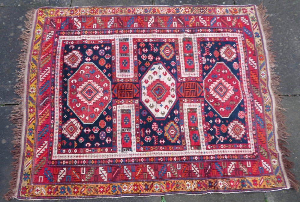 An antique late 19th-century Caucasian Kuba Konagkend wool rug featuring red geometric medallions set against a dark navy field with multi-coloured borders. View IV