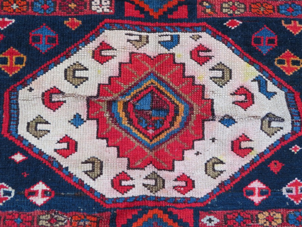 An antique late 19th-century Caucasian Kuba Konagkend wool rug featuring red geometric medallions set against a dark navy field with multi-coloured borders. View VIII
