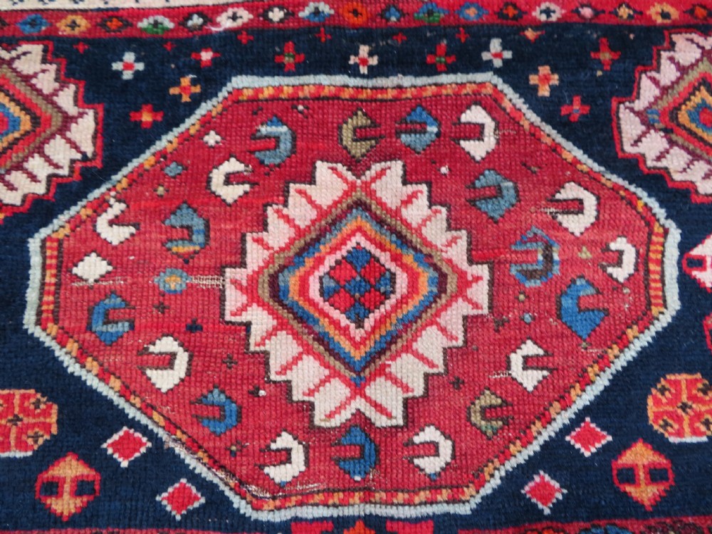 An antique late 19th-century Caucasian Kuba Konagkend wool rug featuring red geometric medallions set against a dark navy field with multi-coloured borders. View IX