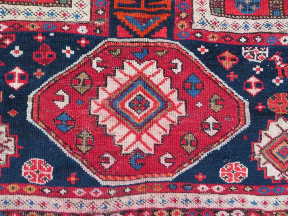 An antique late 19th-century Caucasian Kuba Konagkend wool rug featuring red geometric medallions set against a dark navy field with multi-coloured borders. View X