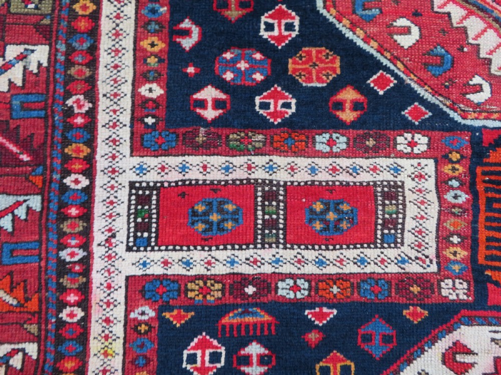 An antique late 19th-century Caucasian Kuba Konagkend wool rug featuring red geometric medallions set against a dark navy field with multi-coloured borders. View XV