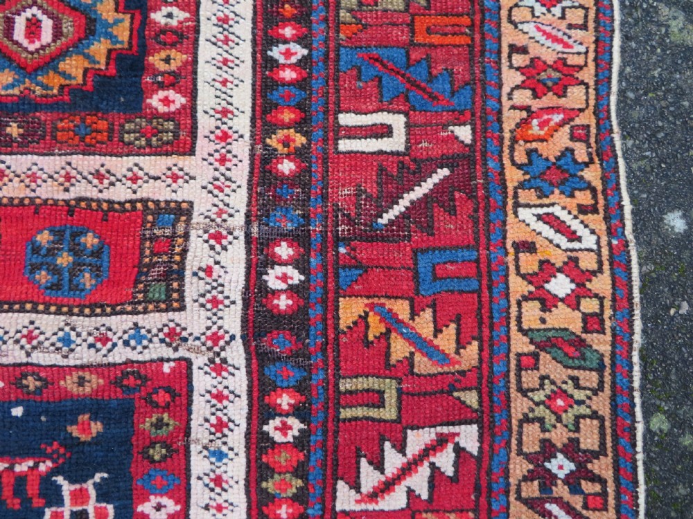 An antique late 19th-century Caucasian Kuba Konagkend wool rug featuring red geometric medallions set against a dark navy field with multi-coloured borders. View XVIII