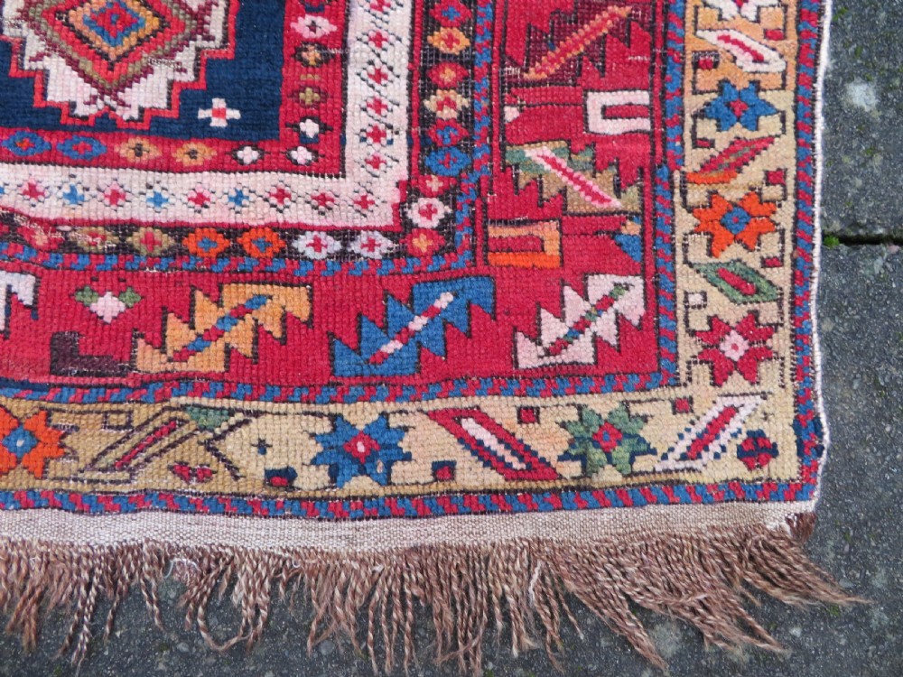 An antique late 19th-century Caucasian Kuba Konagkend wool rug featuring red geometric medallions set against a dark navy field with multi-coloured borders. View XIX