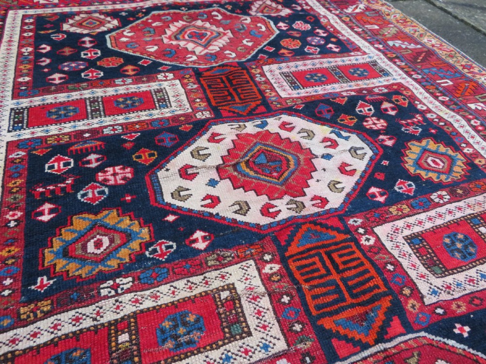 An antique late 19th-century Caucasian Kuba Konagkend wool rug featuring red geometric medallions set against a dark navy field with multi-coloured borders. View XXIV