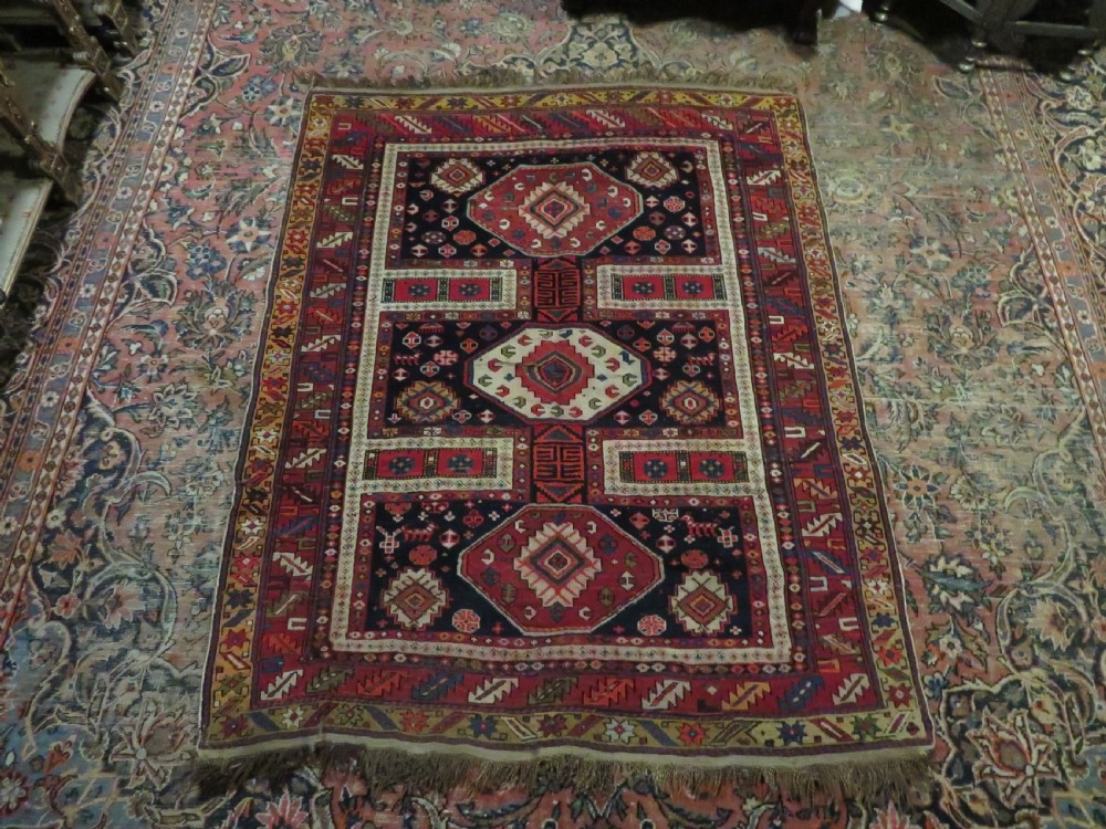 An antique late 19th-century Caucasian Kuba Konagkend wool rug featuring red geometric medallions set against a dark navy field with multi-coloured borders. View XXX