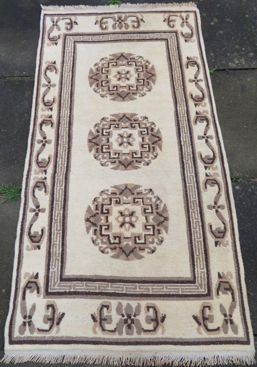 A rectangular hand-knotted wool rug runner featuring three central brown circular medallions on a cream background with a geometric border.