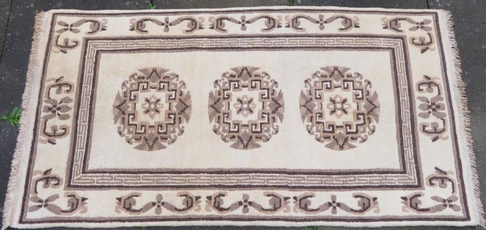 A rectangular hand-knotted wool rug runner featuring three central brown circular medallions on a cream background with a geometric border. View III