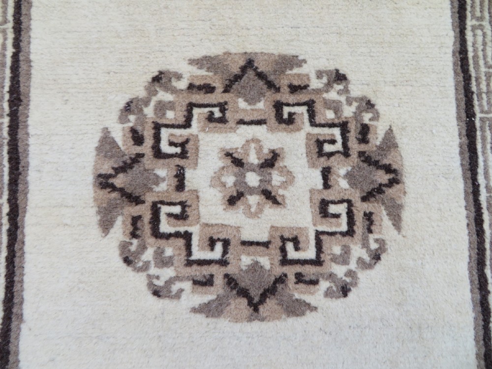 A rectangular hand-knotted wool rug runner featuring three central brown circular medallions on a cream background with a geometric border. View V