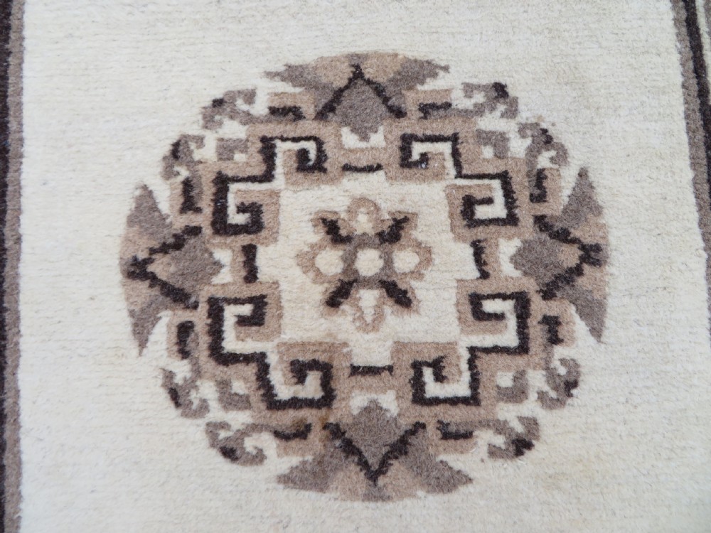 A rectangular hand-knotted wool rug runner featuring three central brown circular medallions on a cream background with a geometric border. View VI