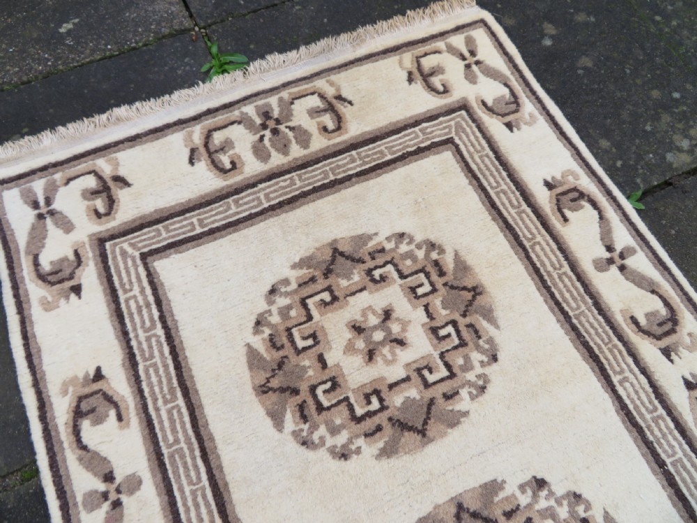 A rectangular hand-knotted wool rug runner featuring three central brown circular medallions on a cream background with a geometric border. View IX