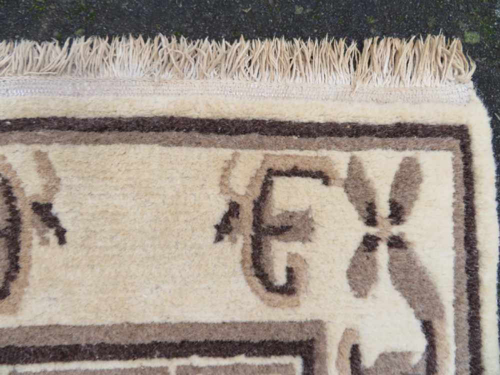 A rectangular hand-knotted wool rug runner featuring three central brown circular medallions on a cream background with a geometric border. View X
