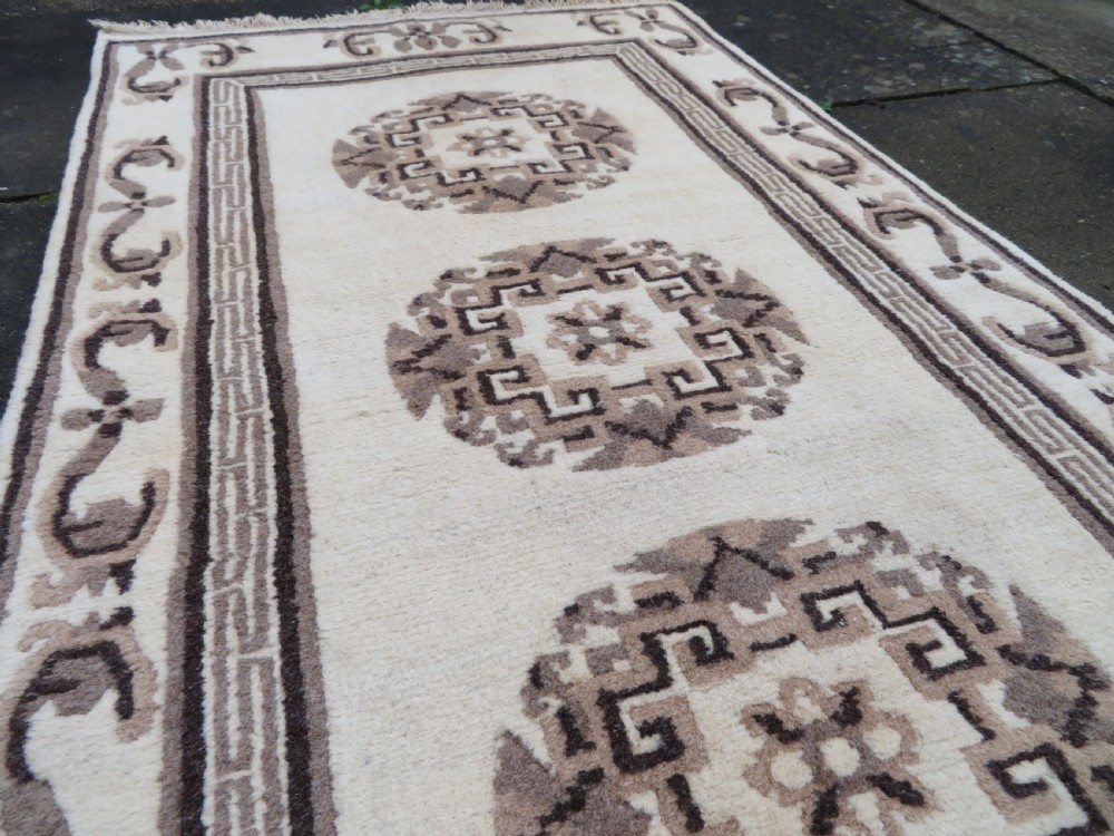 A rectangular hand-knotted wool rug runner featuring three central brown circular medallions on a cream background with a geometric border. View XII