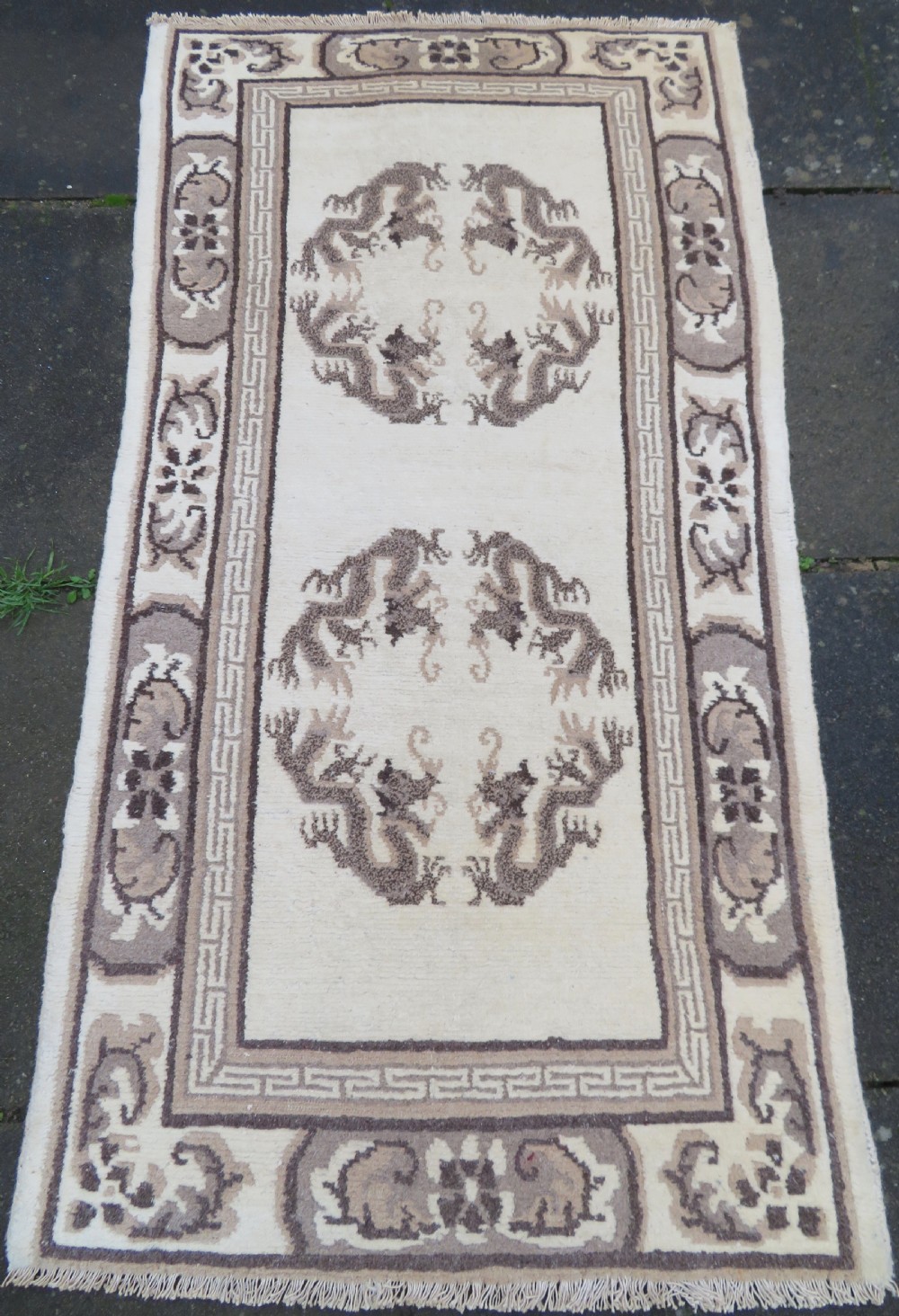 A rectangular hand-knotted cream wool rug featuring two central dragon medallions, a key meander border, and grey decorative motifs.