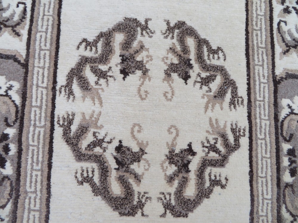 A rectangular hand-knotted cream wool rug featuring two central dragon medallions, a key meander border, and grey decorative motifs. View IV