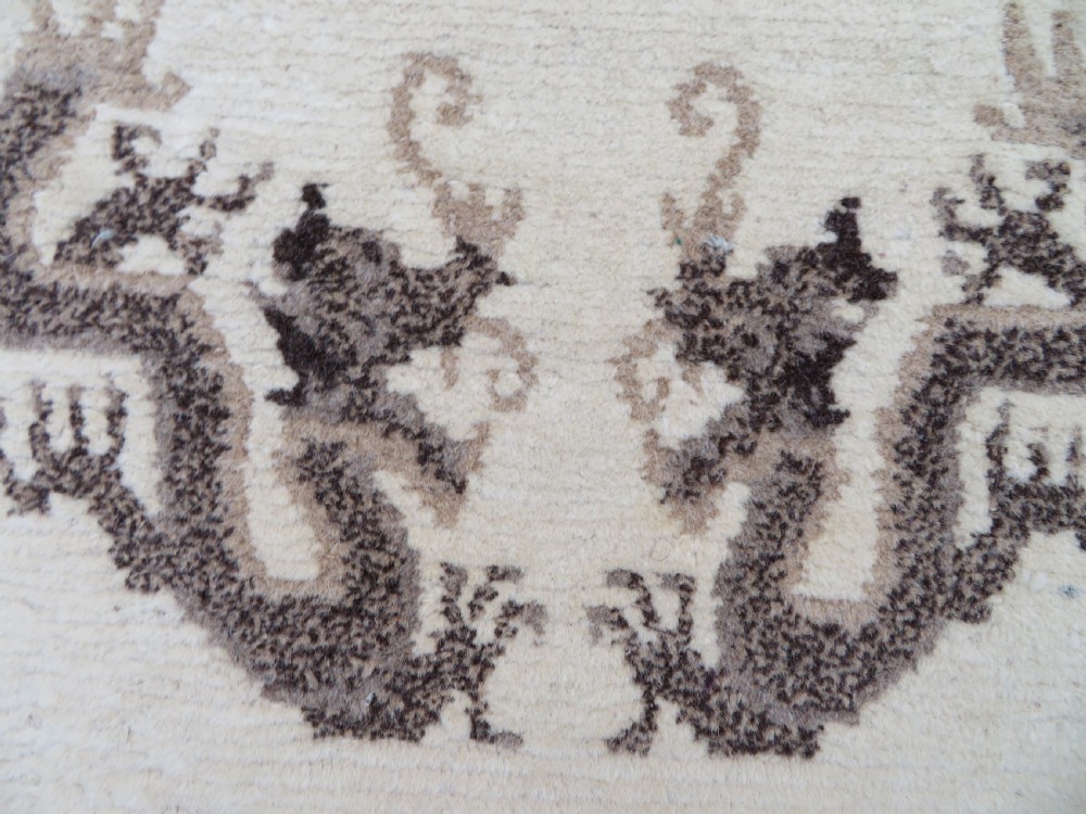 A rectangular hand-knotted cream wool rug featuring two central dragon medallions, a key meander border, and grey decorative motifs. View VII