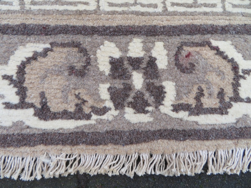 A rectangular hand-knotted cream wool rug featuring two central dragon medallions, a key meander border, and grey decorative motifs. View X