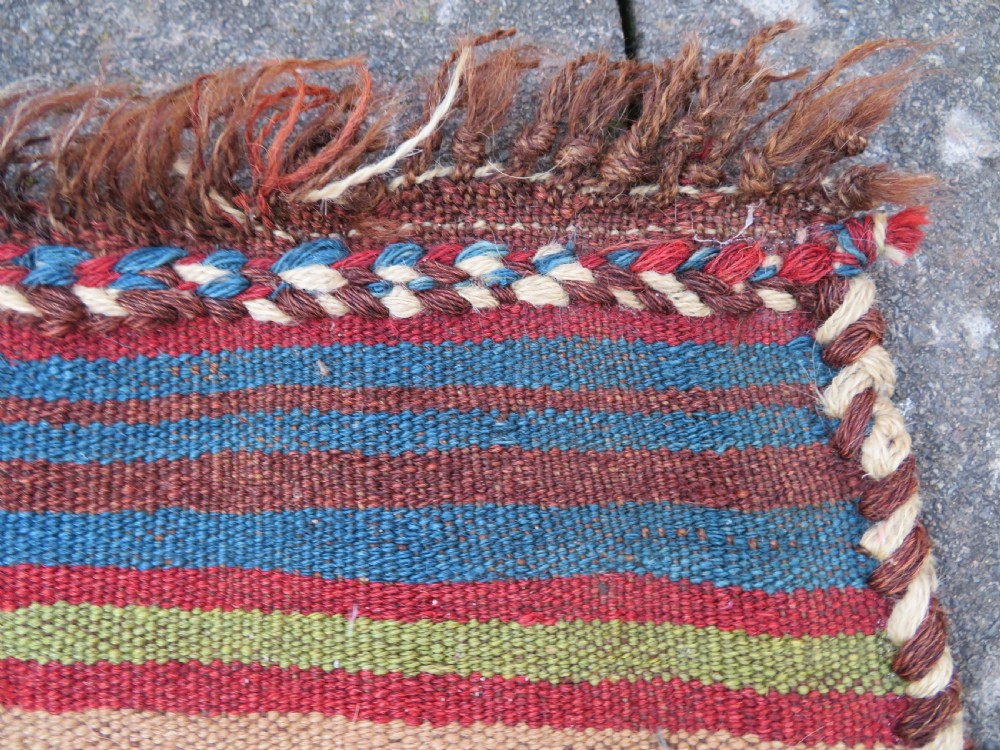 An antique flatweave rug featuring a central undyed tan wool field flanked by colourful horizontal striped end bands and braided fringe edges. View III
