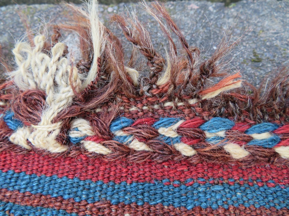 An antique flatweave rug featuring a central undyed tan wool field flanked by colourful horizontal striped end bands and braided fringe edges. View IV