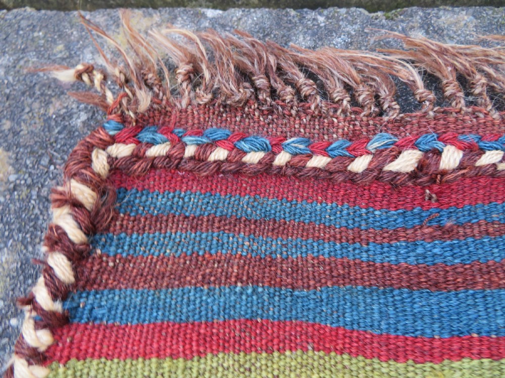 An antique flatweave rug featuring a central undyed tan wool field flanked by colourful horizontal striped end bands and braided fringe edges. View VII