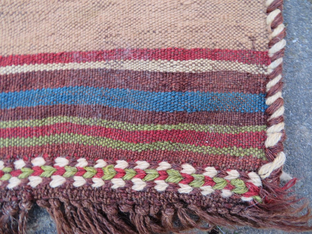 An antique flatweave rug featuring a central undyed tan wool field flanked by colourful horizontal striped end bands and braided fringe edges. View IX