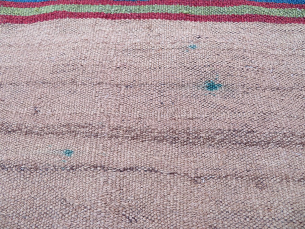 An antique flatweave rug featuring a central undyed tan wool field flanked by colourful horizontal striped end bands and braided fringe edges. View X