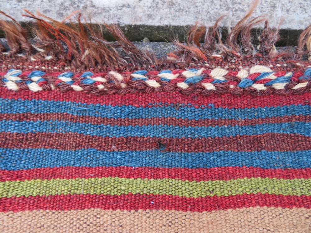 An antique flatweave rug featuring a central undyed tan wool field flanked by colourful horizontal striped end bands and braided fringe edges. View XV
