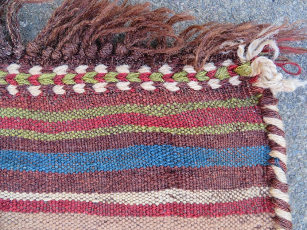 An antique flatweave rug featuring a central undyed tan wool field flanked by colourful horizontal striped end bands and braided fringe edges. View XVI