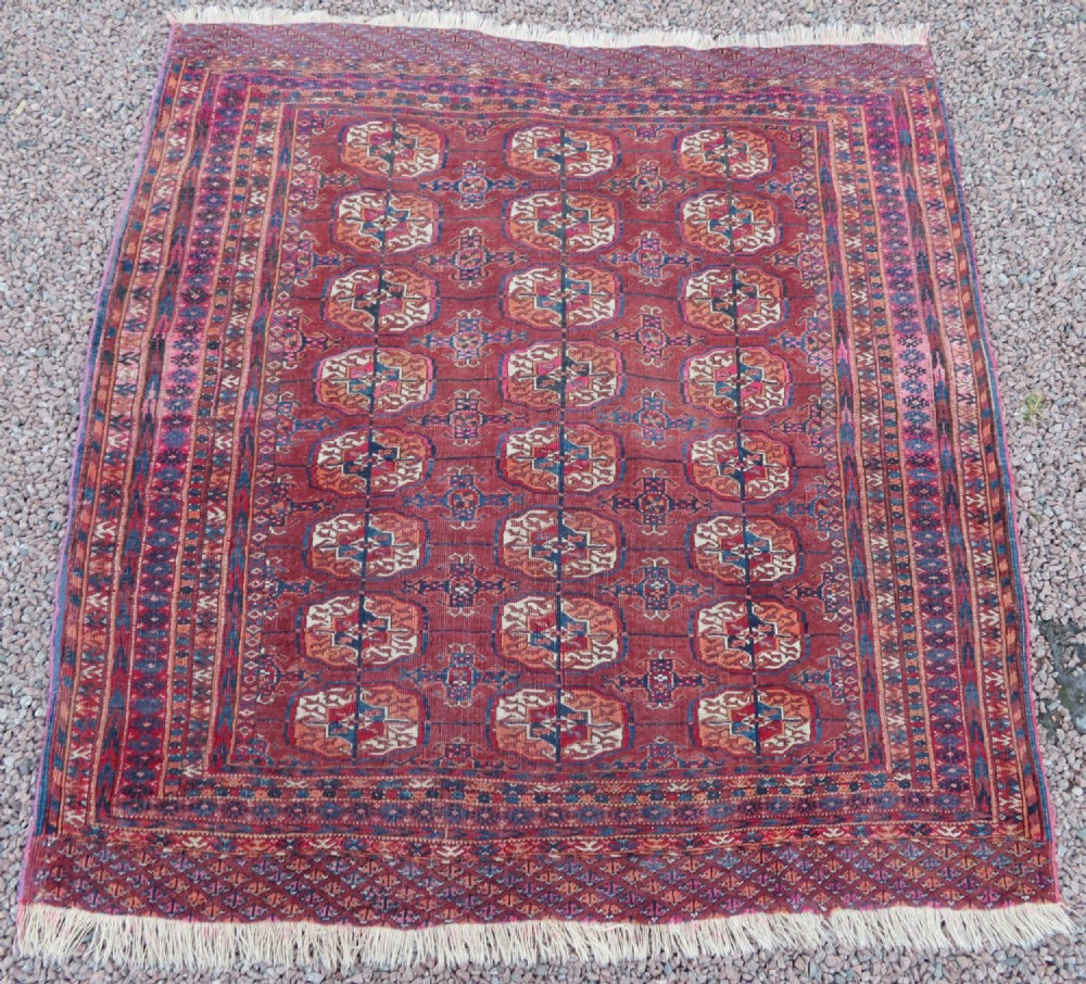An antique Tekke Turkmen hand-knotted wool rug featuring repeating geometric gul patterns across a deep red field framed by multiple ornamental borders.