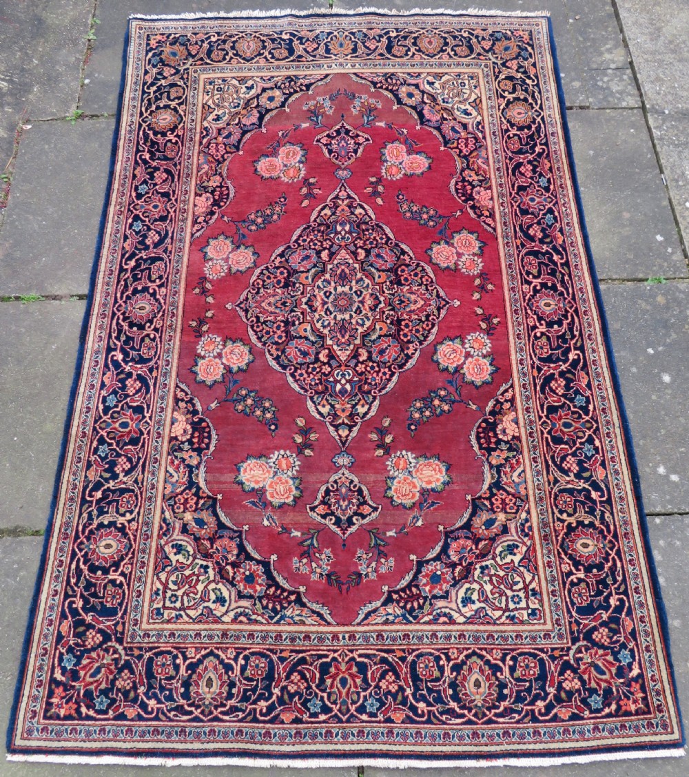 A hand-knotted Persian Kashan wool rug featuring a central navy and cream floral medallion on a rose pink field surrounded by floral spandrels and a navy border.