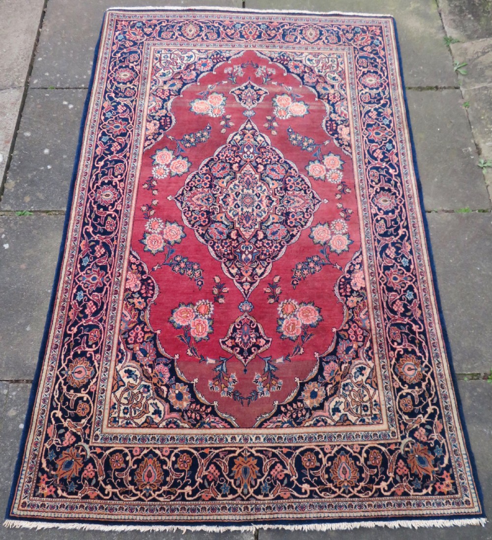 A hand-knotted Persian Kashan wool rug featuring a central navy and cream floral medallion on a rose pink field surrounded by floral spandrels and a navy border. View II