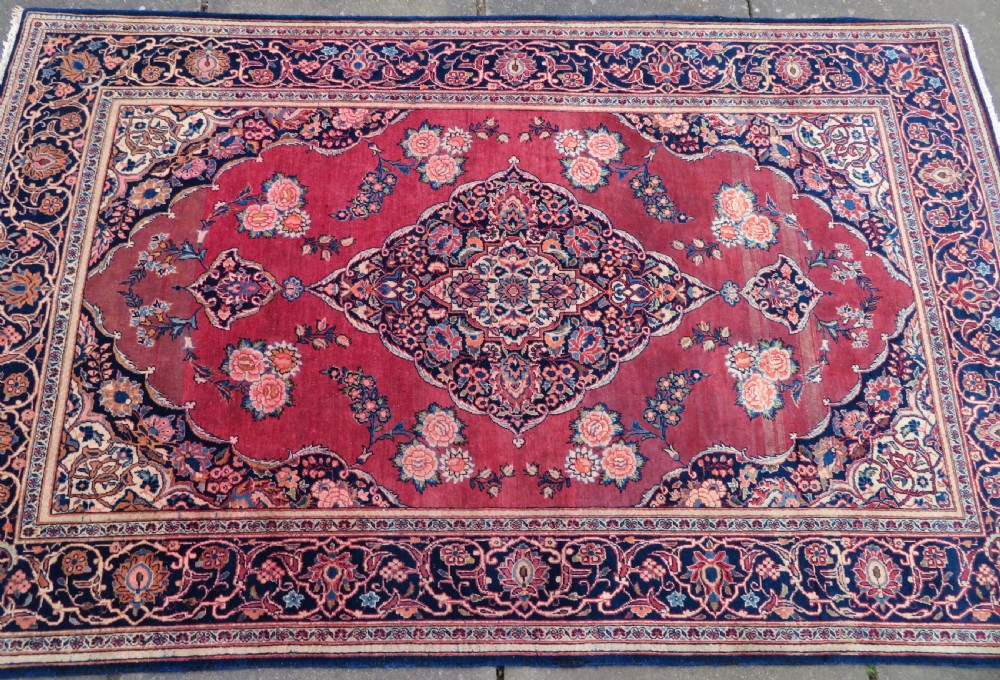 A hand-knotted Persian Kashan wool rug featuring a central navy and cream floral medallion on a rose pink field surrounded by floral spandrels and a navy border. View III