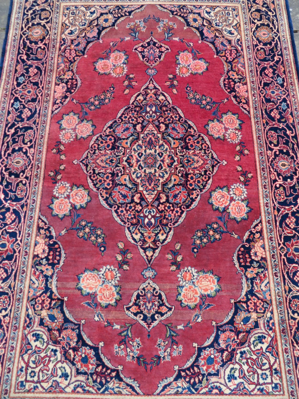 A hand-knotted Persian Kashan wool rug featuring a central navy and cream floral medallion on a rose pink field surrounded by floral spandrels and a navy border. View IV