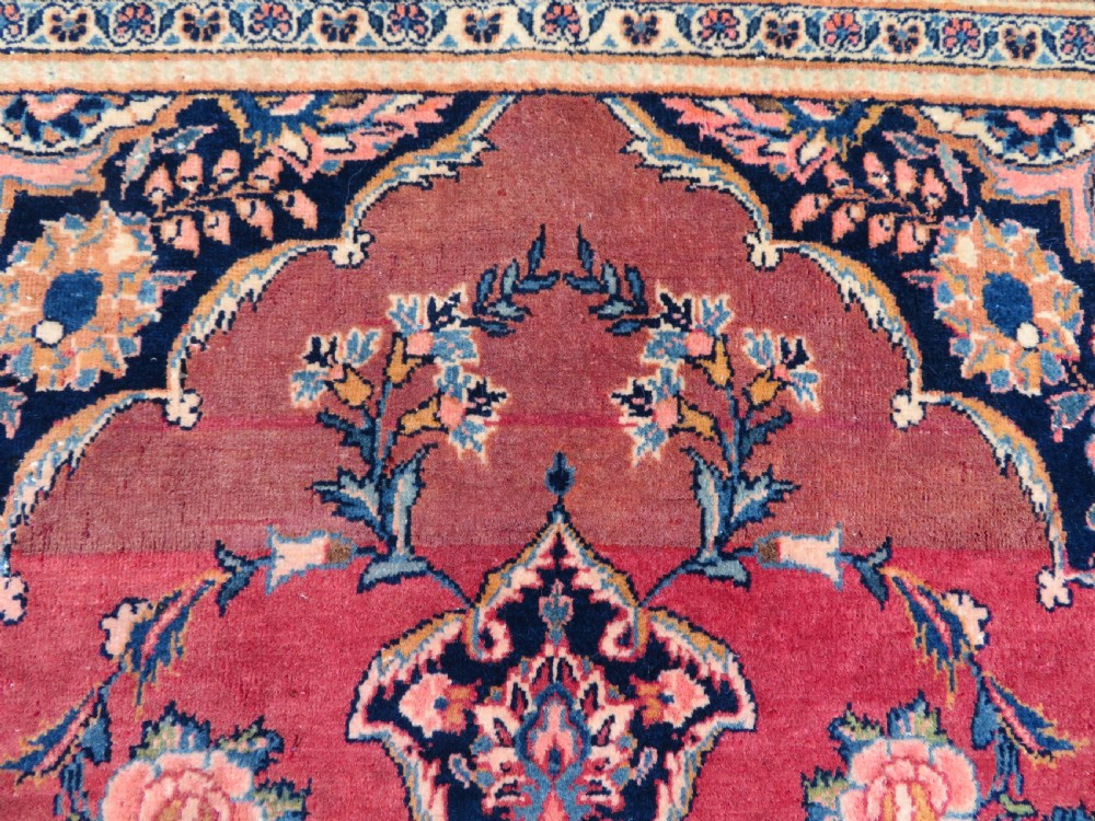 A hand-knotted Persian Kashan wool rug featuring a central navy and cream floral medallion on a rose pink field surrounded by floral spandrels and a navy border. View V