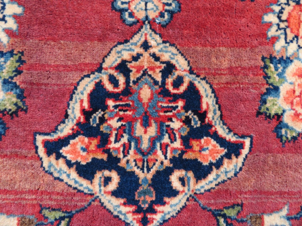 A hand-knotted Persian Kashan wool rug featuring a central navy and cream floral medallion on a rose pink field surrounded by floral spandrels and a navy border. View IX