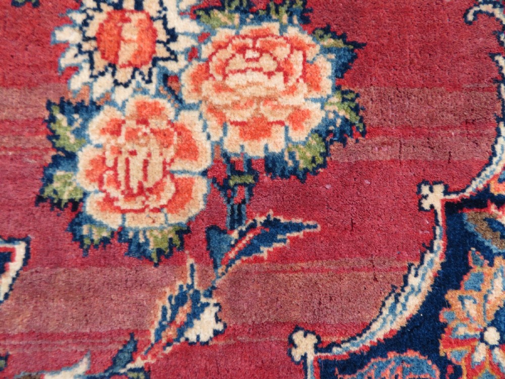 A hand-knotted Persian Kashan wool rug featuring a central navy and cream floral medallion on a rose pink field surrounded by floral spandrels and a navy border. View X