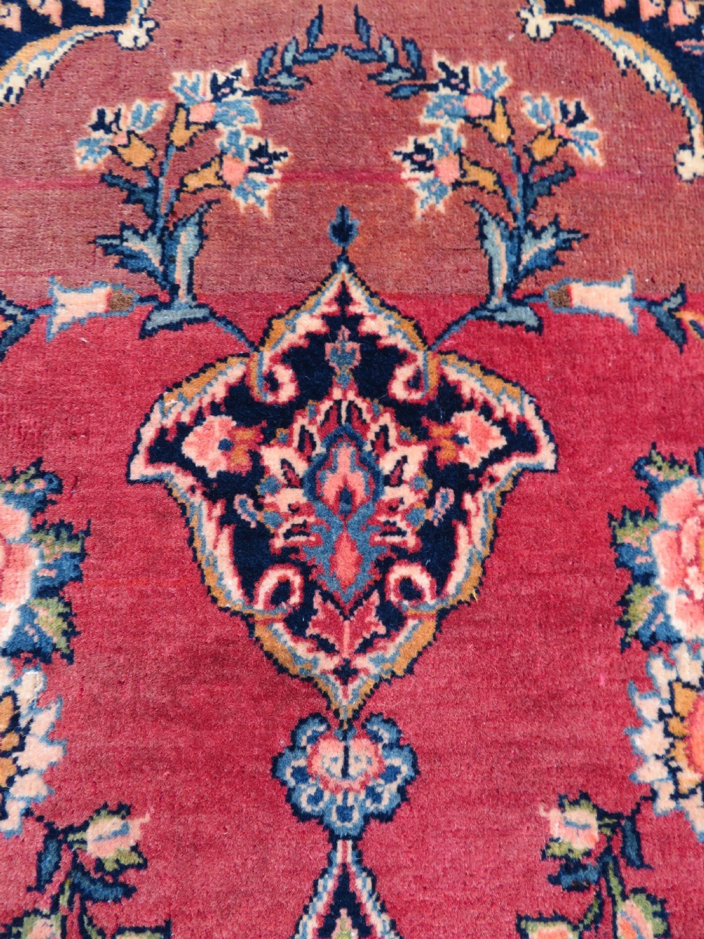A hand-knotted Persian Kashan wool rug featuring a central navy and cream floral medallion on a rose pink field surrounded by floral spandrels and a navy border. View XII