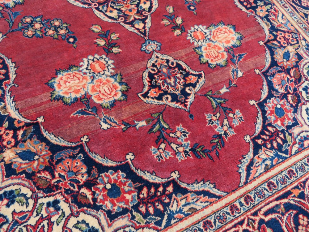 A hand-knotted Persian Kashan wool rug featuring a central navy and cream floral medallion on a rose pink field surrounded by floral spandrels and a navy border. View XVII
