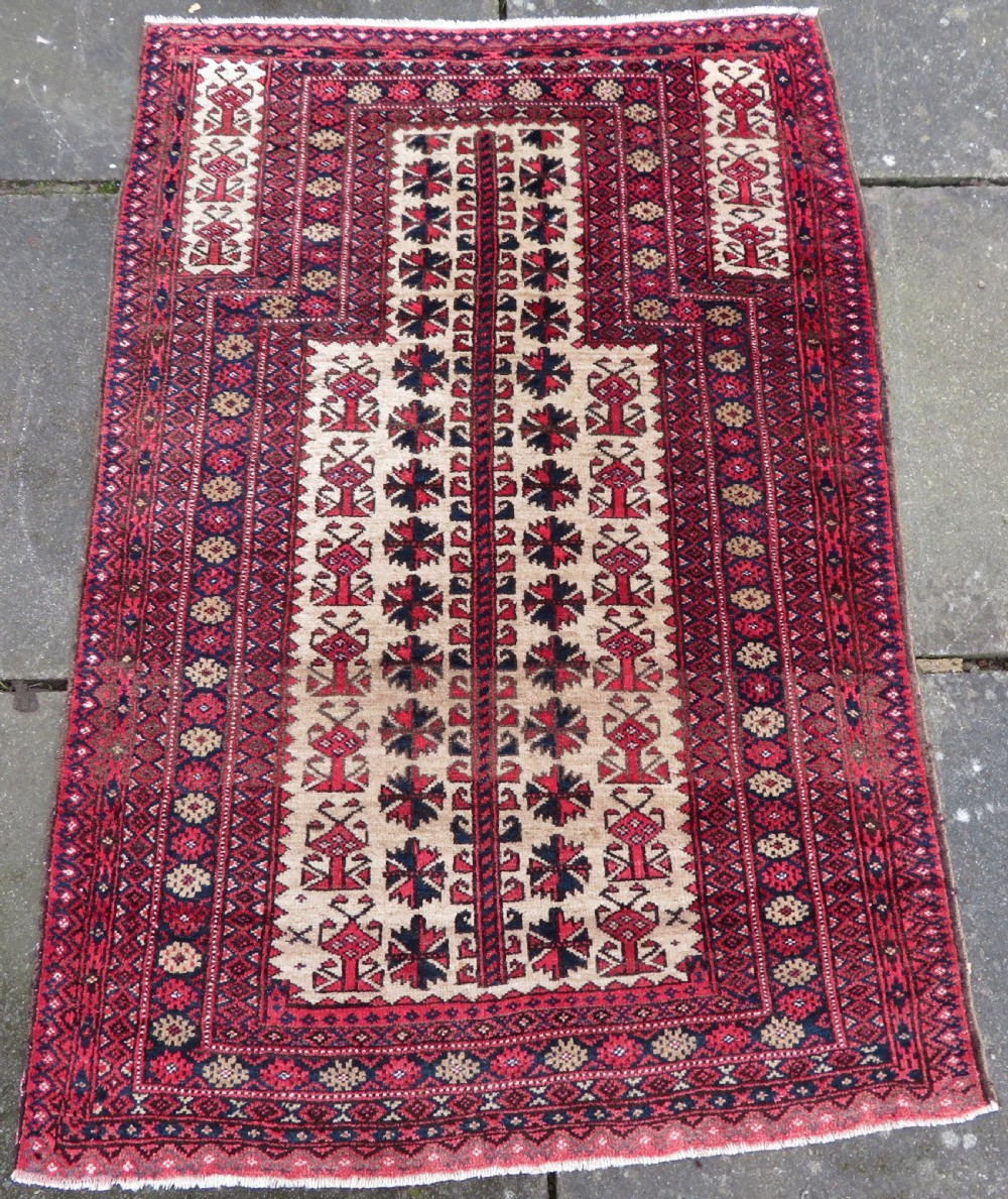 An antique hand-knotted Baluch wool rug featuring a central tree of life design on a cream field surrounded by red and navy geometric borders.