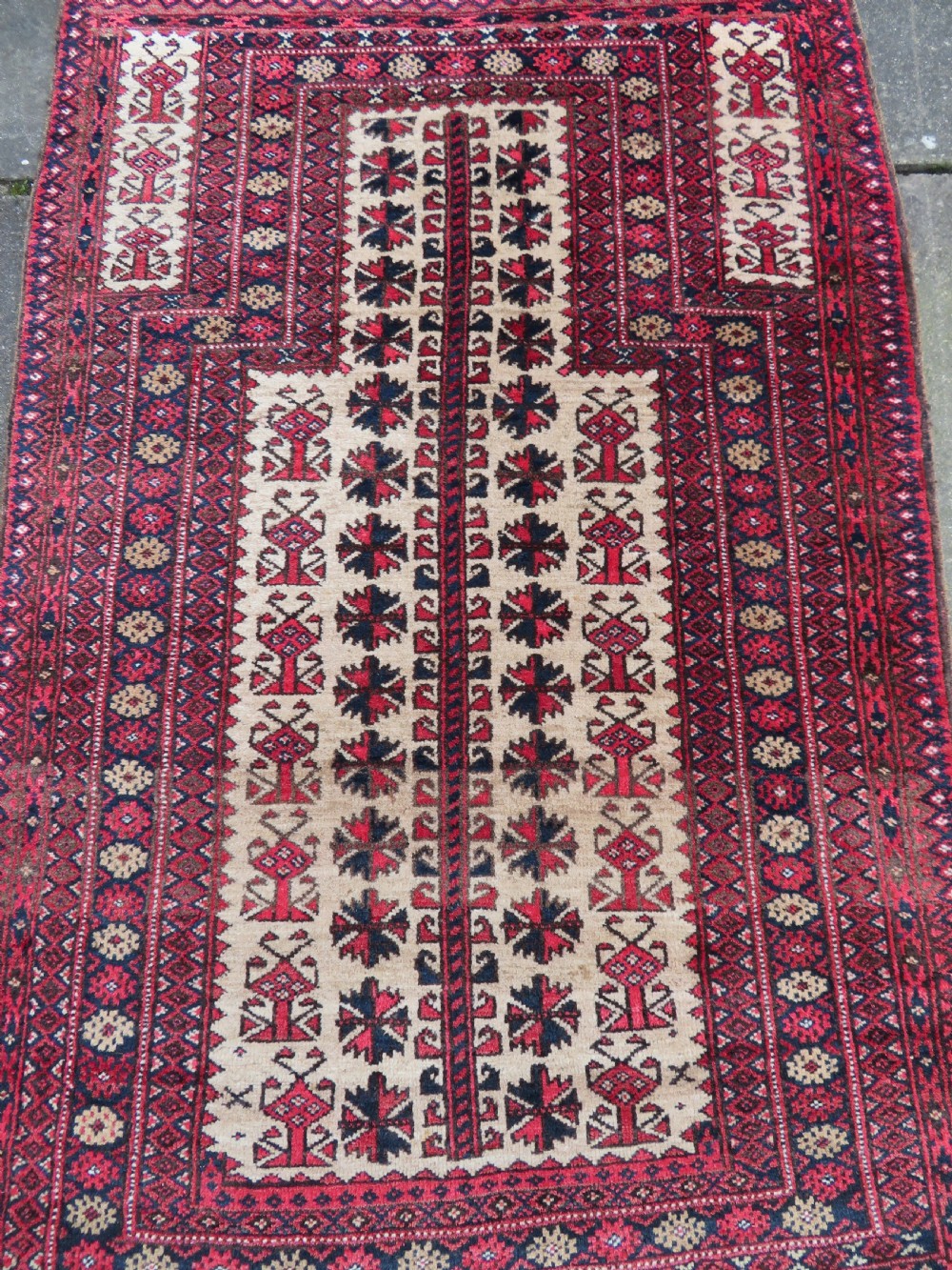 An antique hand-knotted Baluch wool rug featuring a central tree of life design on a cream field surrounded by red and navy geometric borders. View IV