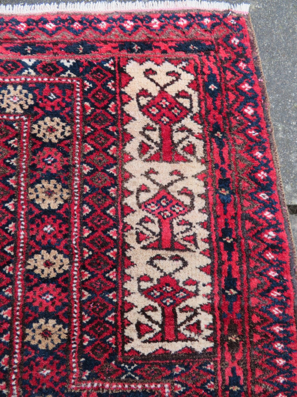 An antique hand-knotted Baluch wool rug featuring a central tree of life design on a cream field surrounded by red and navy geometric borders. View VI