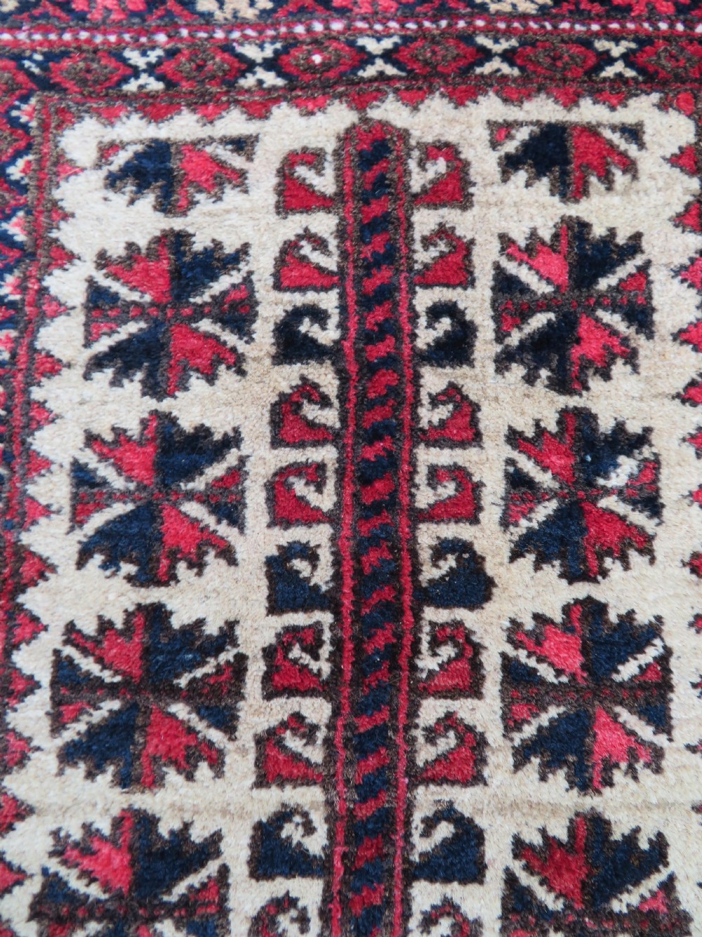 An antique hand-knotted Baluch wool rug featuring a central tree of life design on a cream field surrounded by red and navy geometric borders. View VII