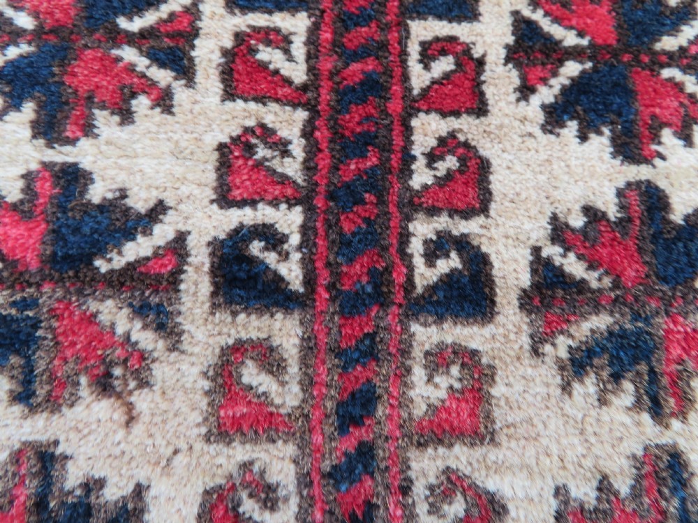 An antique hand-knotted Baluch wool rug featuring a central tree of life design on a cream field surrounded by red and navy geometric borders. View VIII