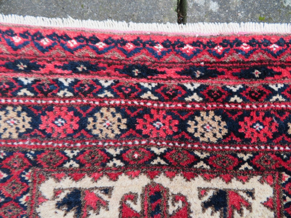 An antique hand-knotted Baluch wool rug featuring a central tree of life design on a cream field surrounded by red and navy geometric borders. View XII