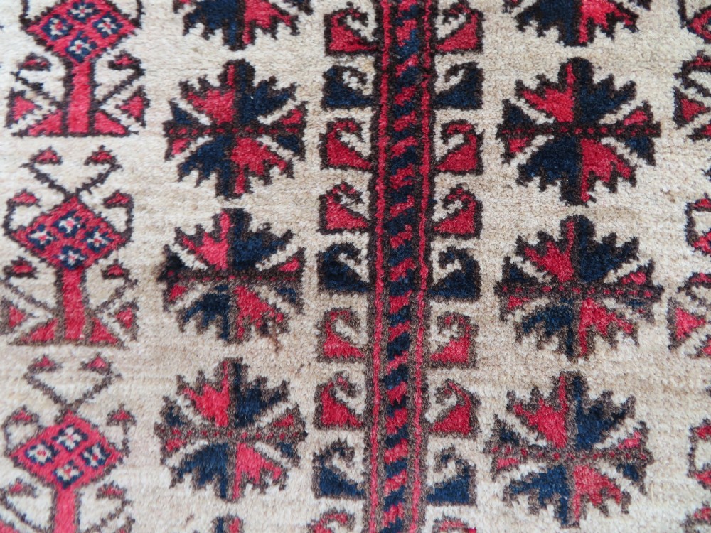 An antique hand-knotted Baluch wool rug featuring a central tree of life design on a cream field surrounded by red and navy geometric borders. View XVI