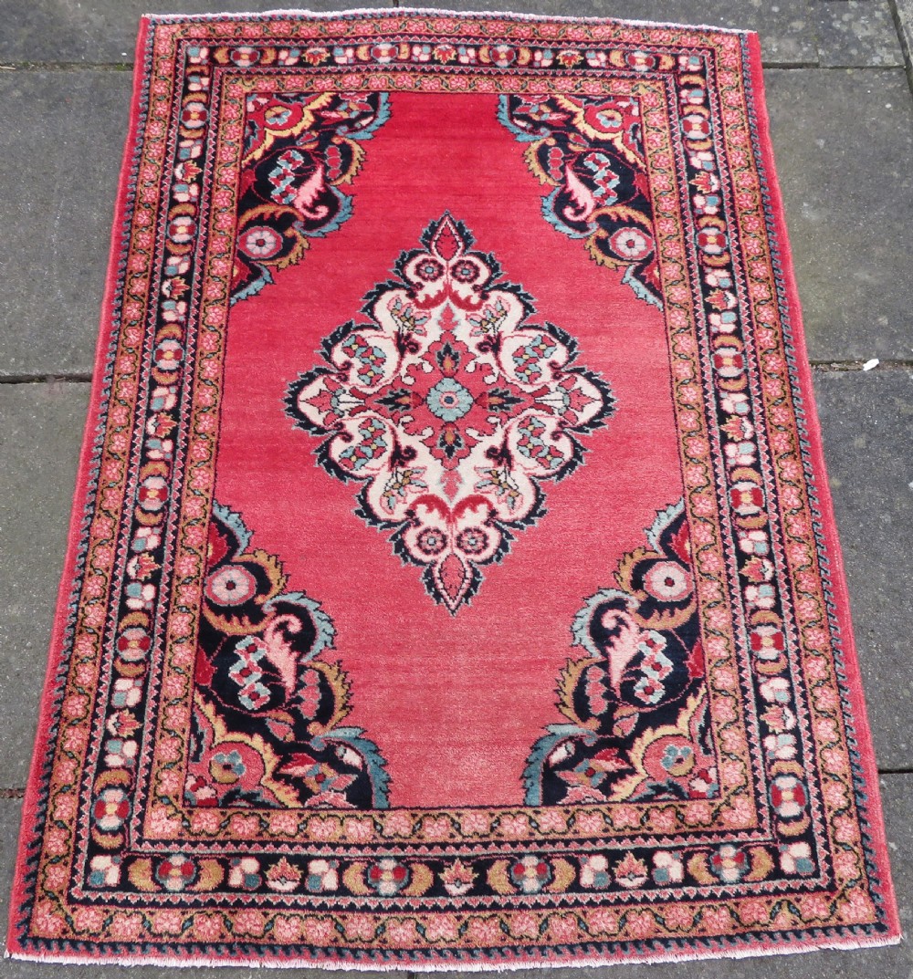 An antique Jozan Persian rug featuring a central floral medallion on a rose red field surrounded by intricate spandrels and multi-band patterned borders.