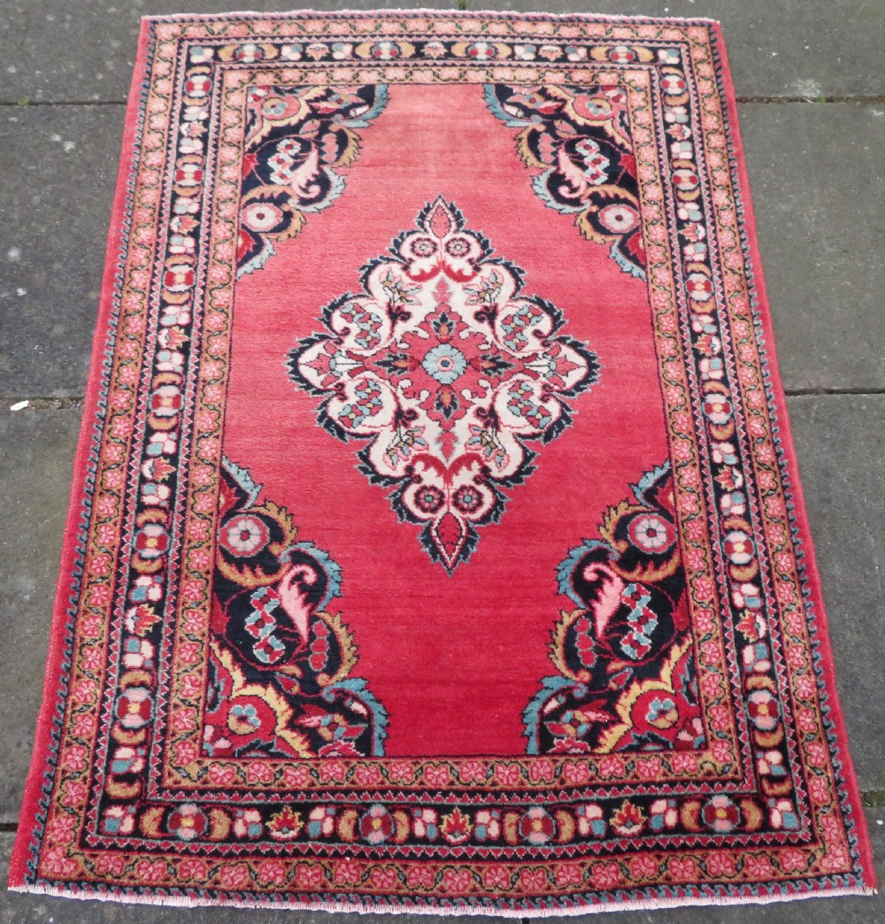 An antique Jozan Persian rug featuring a central floral medallion on a rose red field surrounded by intricate spandrels and multi-band patterned borders. View II